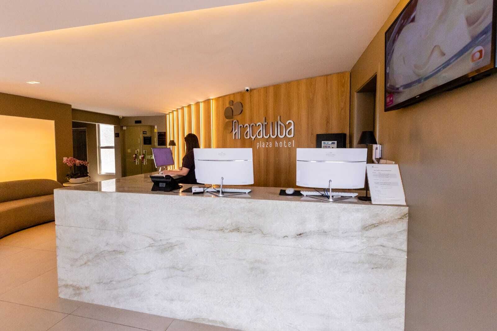 Un comptoir d’accueil à l’hôtel Iracauba Plaza, avec un mur en bois et deux écrans d’ordinateur.