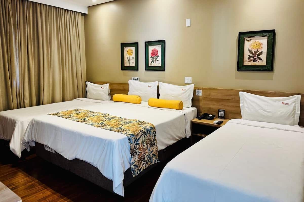 A hotel room with two single beds, a large bed, and a nightstand with a phone.
