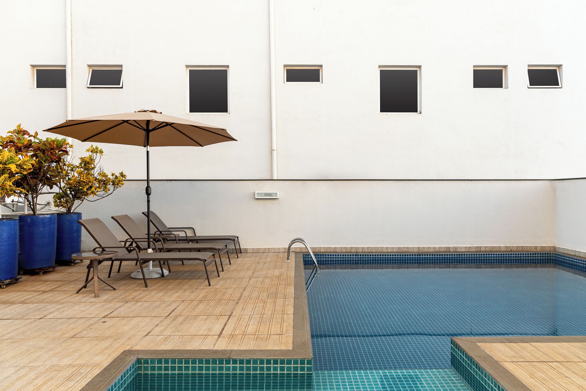 Una piscina con tumbonas y una sombrilla, rodeada por una terraza de baldosas.