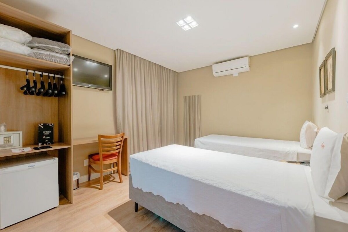 Une chambre d’hôtel avec deux lits, un bureau, une chaise et une armoire.