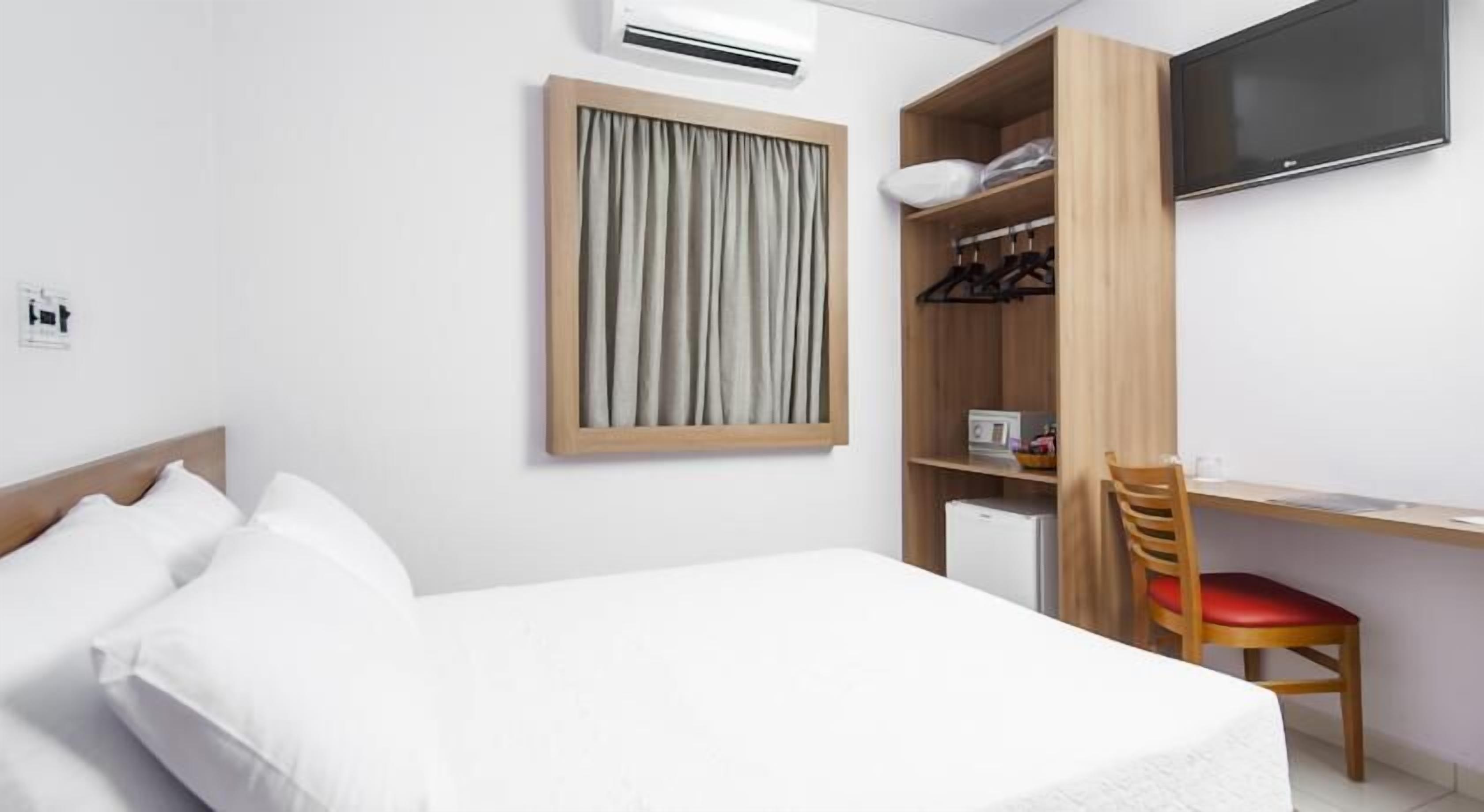 Habitació d'hotel amb llit, escriptori, cadira, televisió i armari.