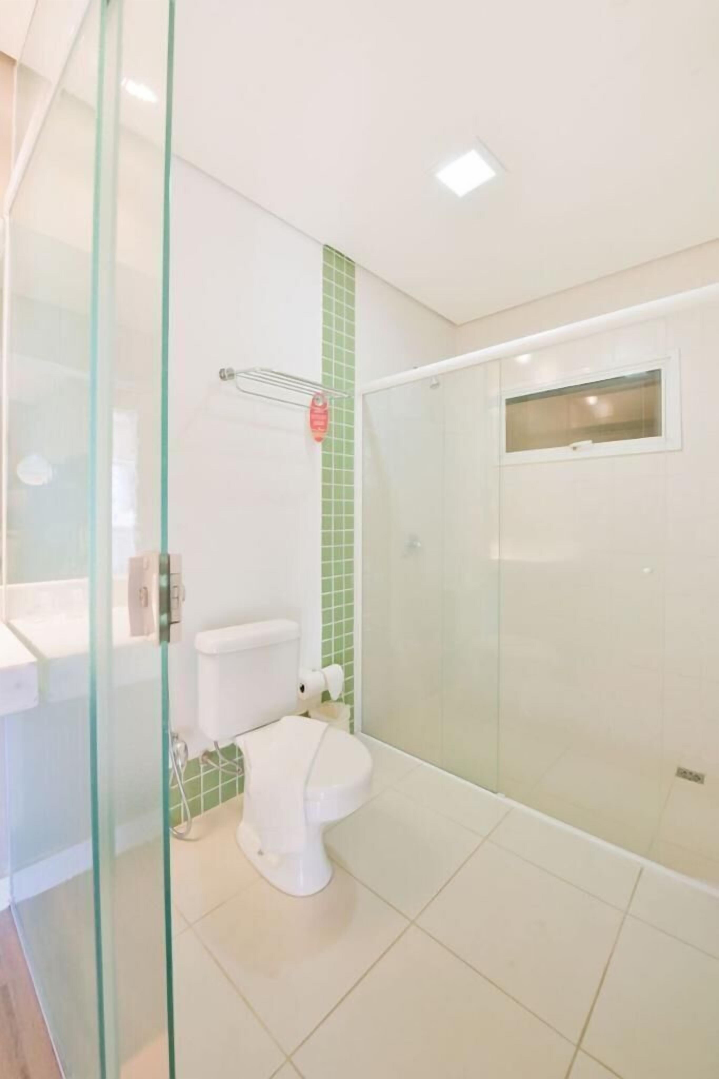 Une salle de bain moderne avec une douche à parois de verre, des toilettes blanches et un mur recouvert de carreaux verts.