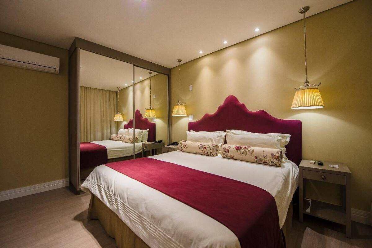 A hotel room with a large bed, a nightstand, a mirror, and a hanging lamp.