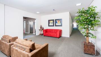 Un amplio espacio de oficina con un sofá rojo, dos sillones, una planta en maceta y obras de arte en las paredes.