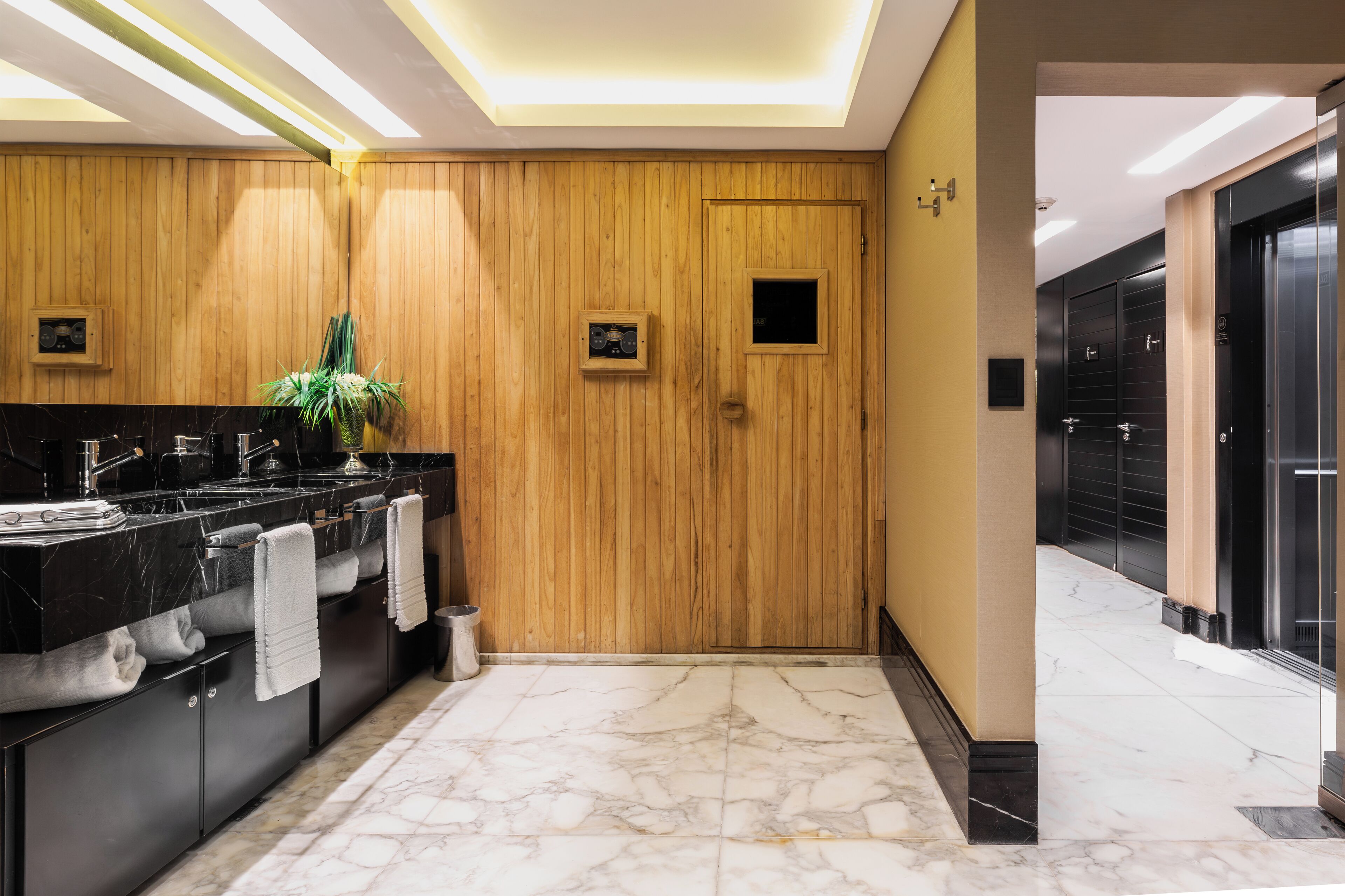 A modern bathroom with wooden paneling, a marble floor, and a black sink with multiple faucets.