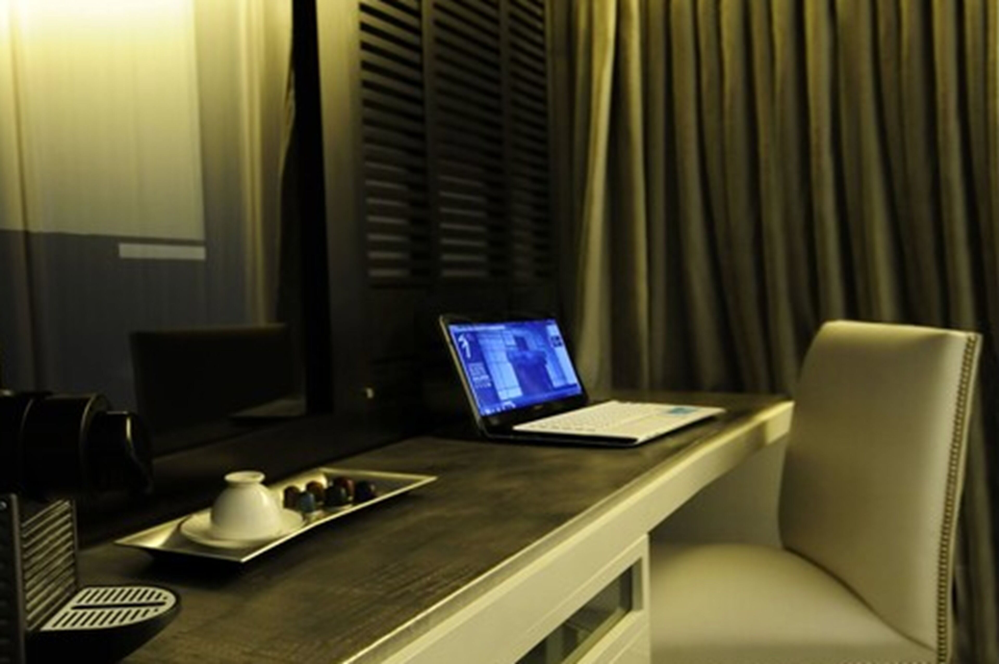 A hotel room with a desk, laptop, and a tray with a teapot and cups.