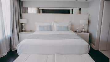 A modern hotel bedroom with a large bed, two bedside tables with lamps, a headboard, and a view of the outside through a window.