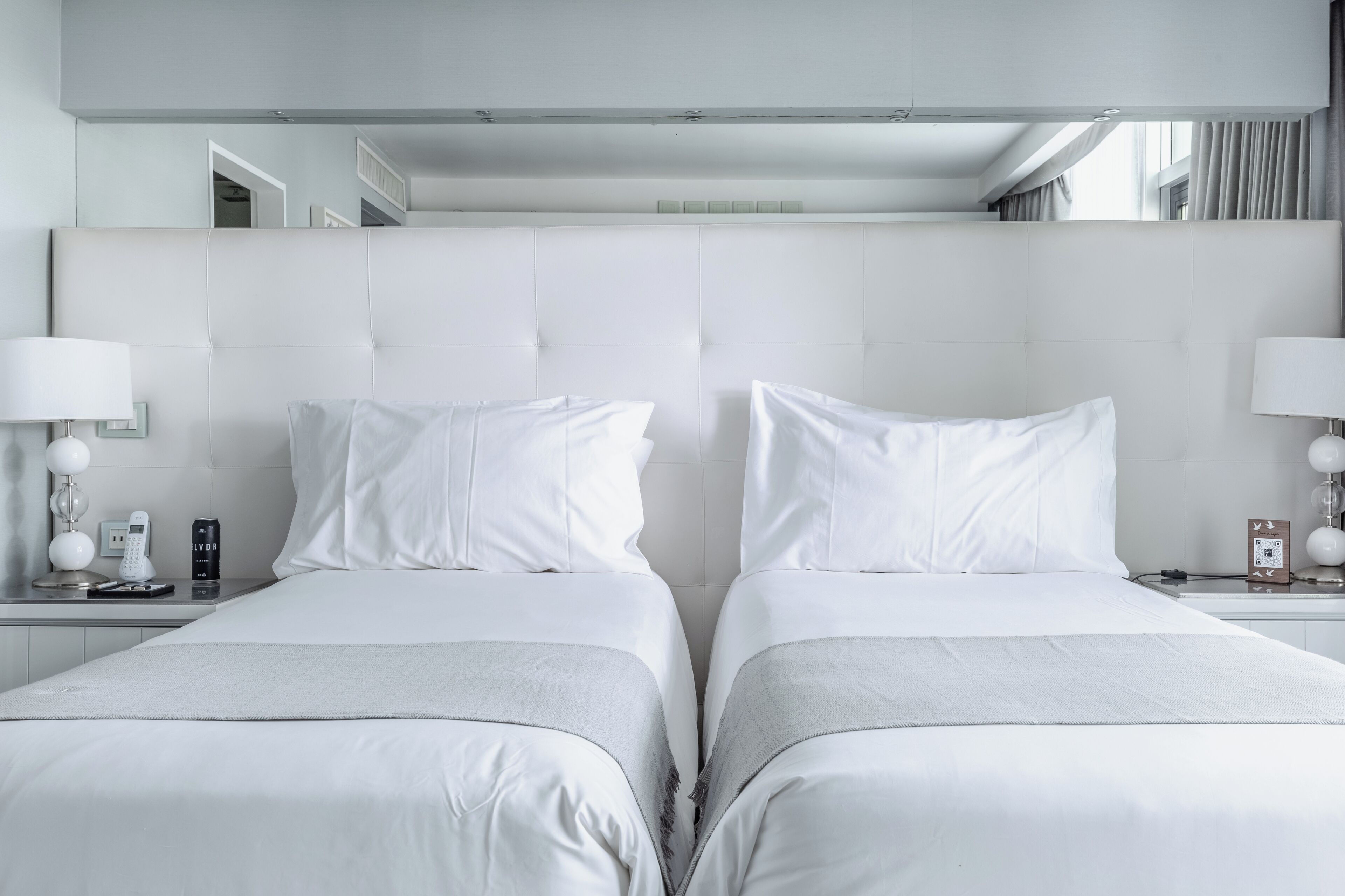 A modern hotel room with a large bed, bedside tables, and a mirror above the bed.