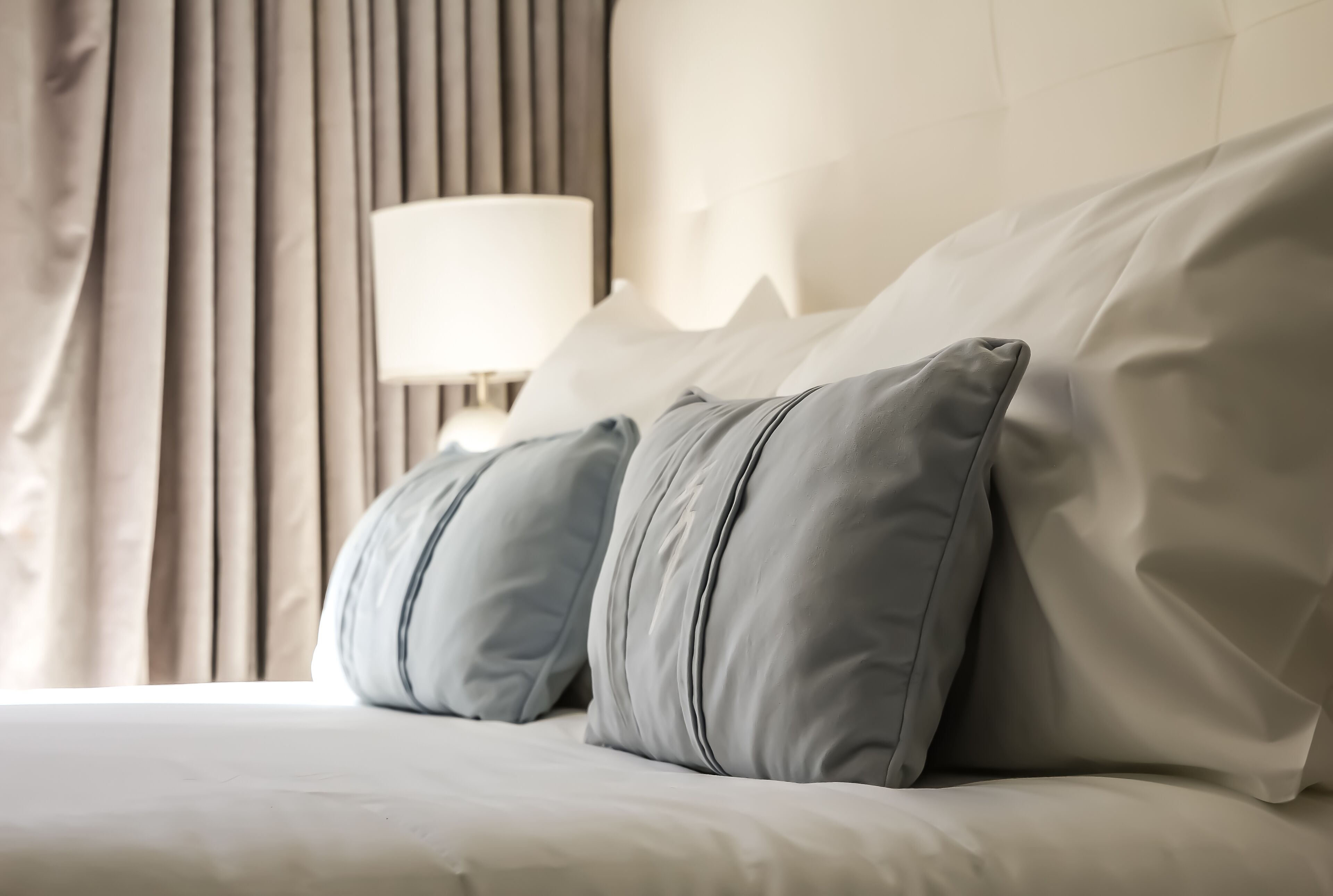 A neatly made bed with grey pillows and a white headboard in a hotel room.