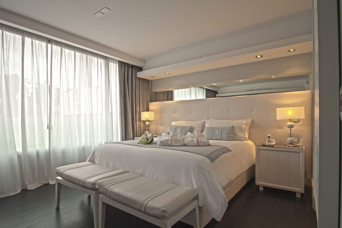 A modern hotel room with a large bed, bedside tables, a bench, and a view of the outdoors.