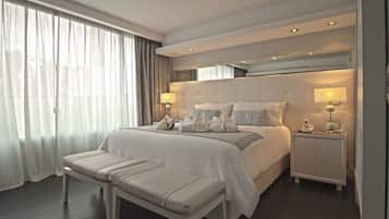A modern hotel room with a large bed, bedside tables, a bench, and a view of the outdoors.