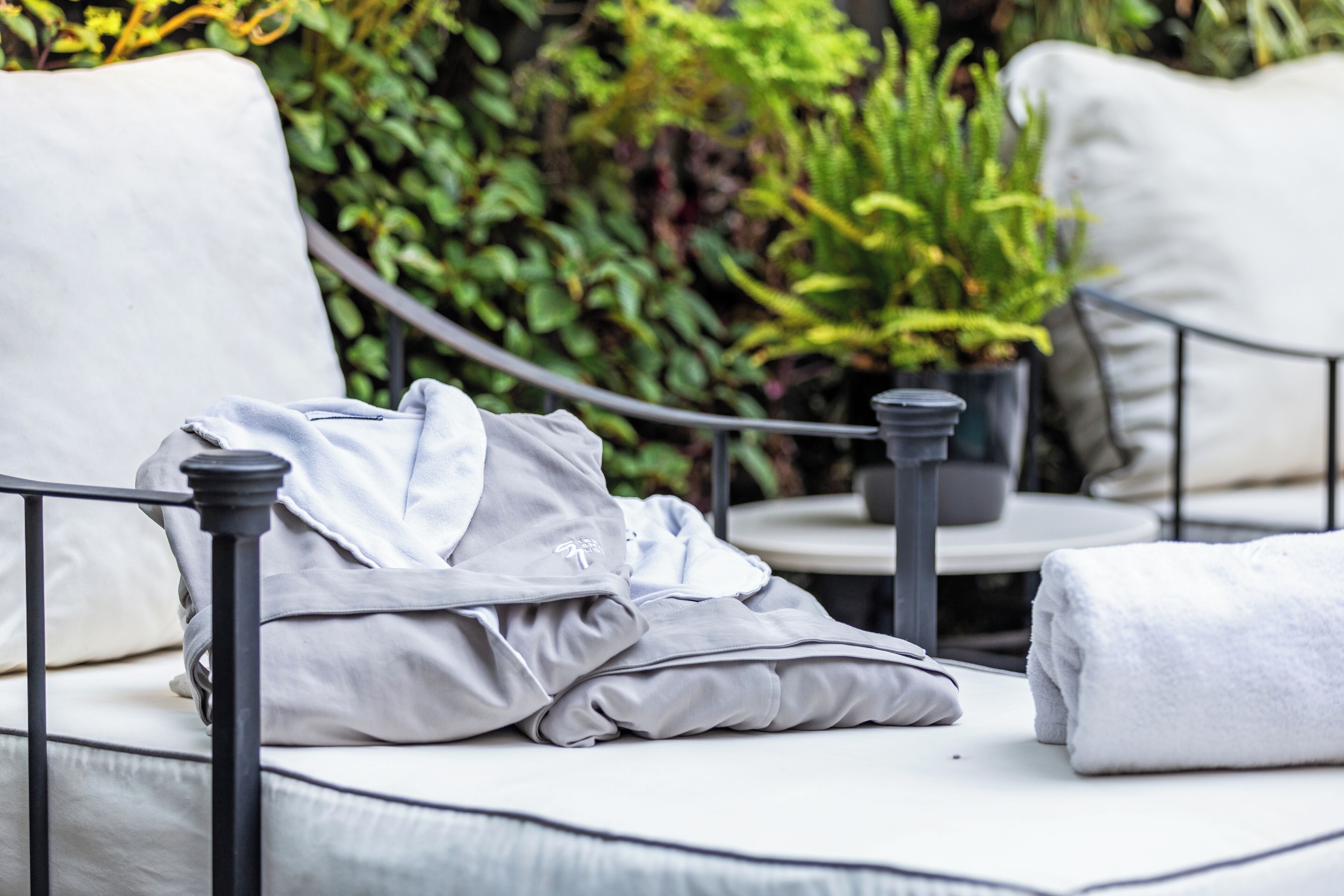 A white outdoor seating area with a metal railing, a white cushioned bench, and a potted plant.