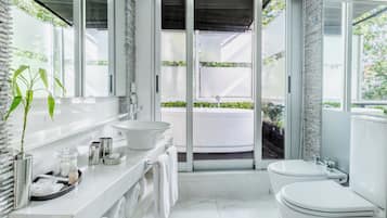 Un baño moderno con un tocador blanco, un espejo grande, un inodoro blanco y una bañera visible a través de una puerta de cristal.