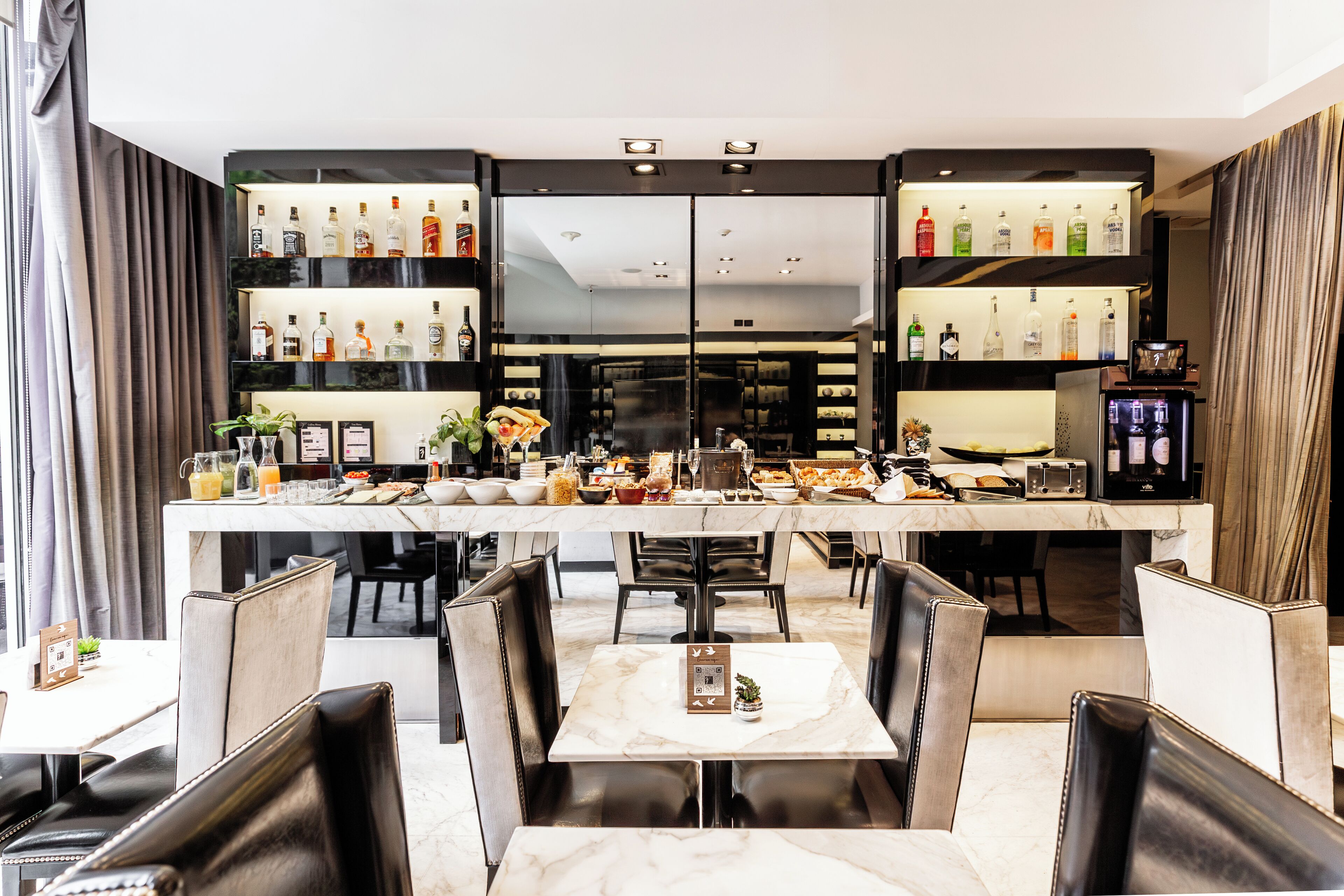 A restaurant with a bar area, marble tables, and leather chairs.