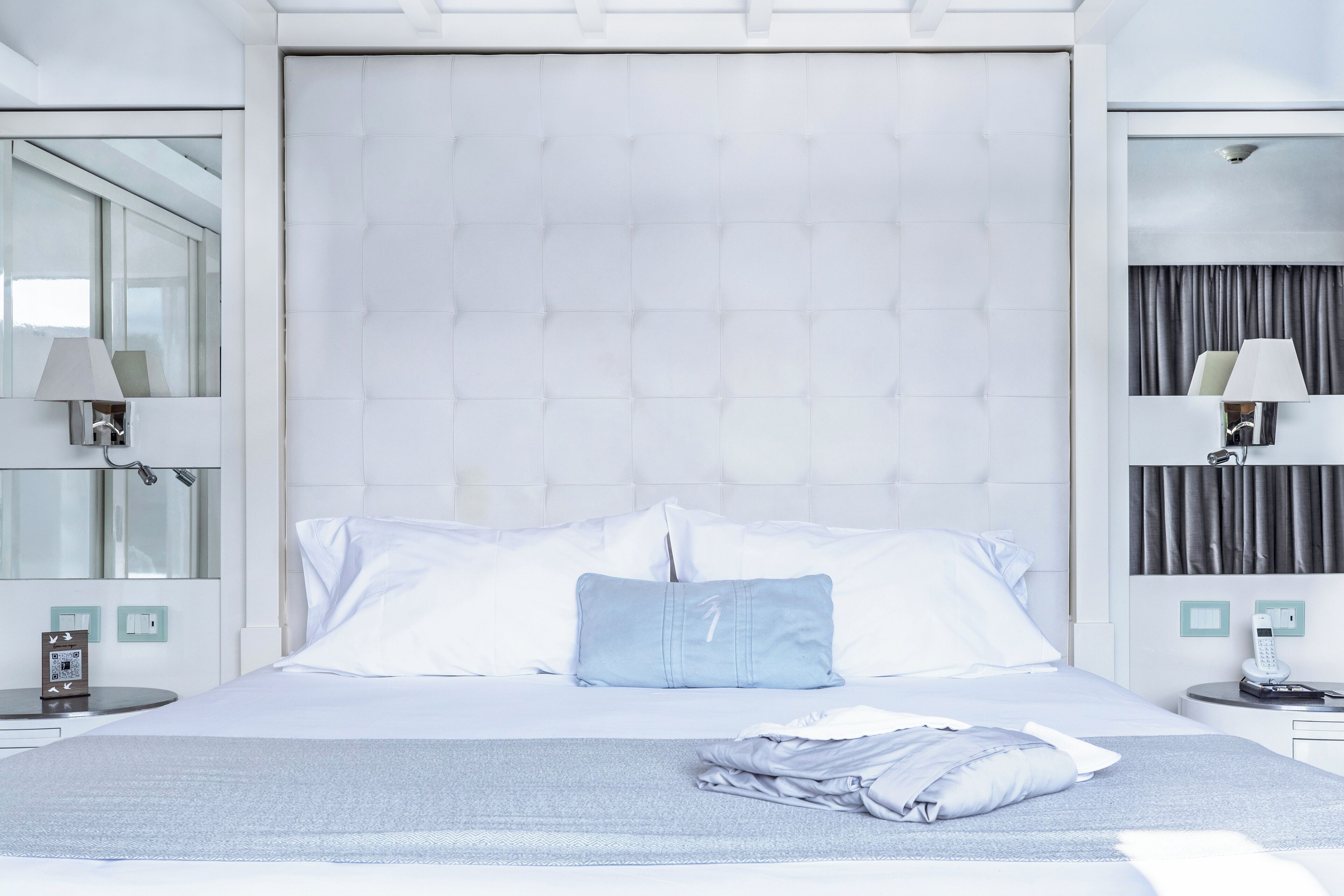 Habitació d'hotel moderna amb un llit gran, una taula de nit, una làmpada i una finestra amb cortines.