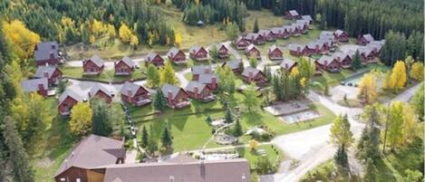 A cluster of red-roofed cabins arranged in rows, surrounded by a forested area with autumn foliage.
