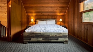 A wooden-paneled room with a bed, two bedside lamps, and a window with a view of trees. - Banff Gate Mountain Resort (Canmore)
