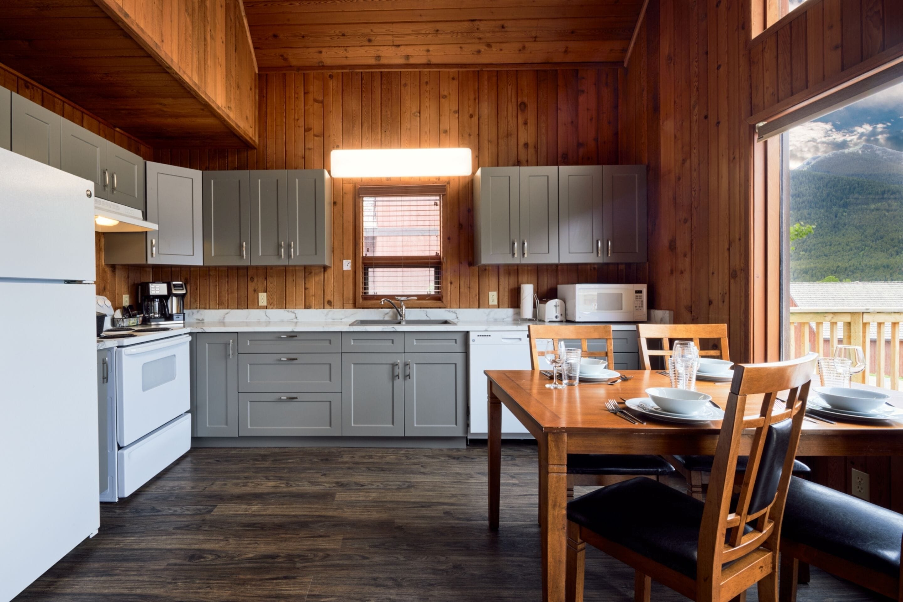 A wooden cabin-style kitchen with grey cabinets, a white refrigerator, and a dining table set for four.