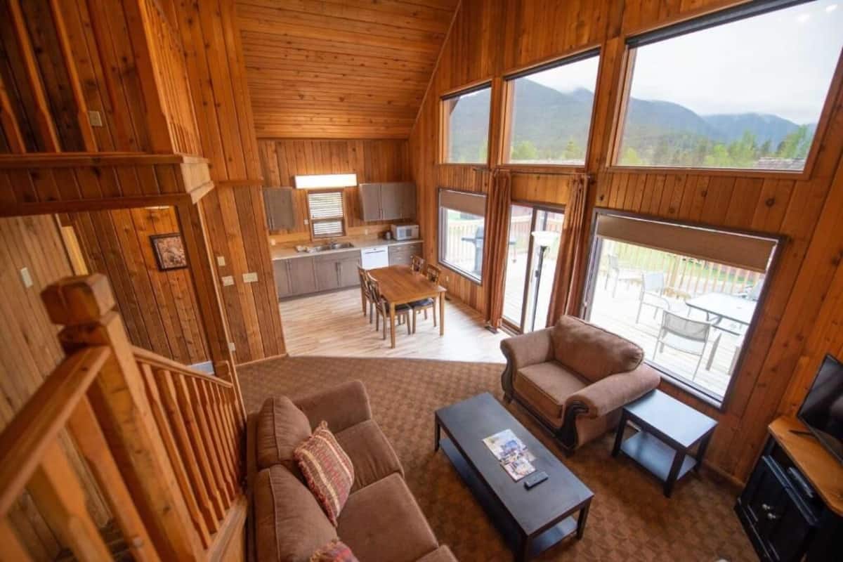 A wooden cabin interior with a dining area, kitchen, and a sofa set.