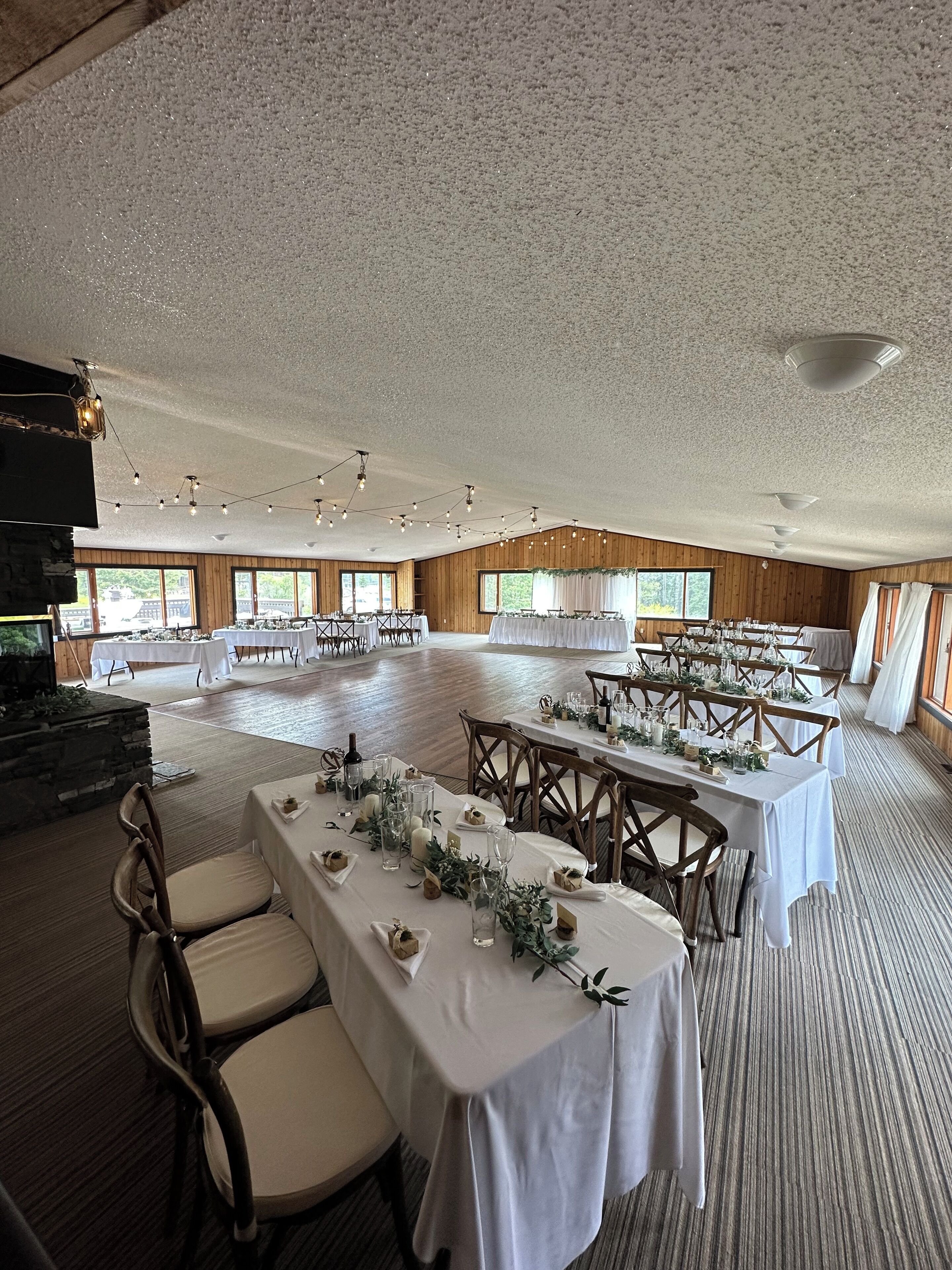 Un salón amplio con varias mesas dispuestas para comer, paneles de madera en las paredes y grandes ventanales que dejan entrar luz natural.