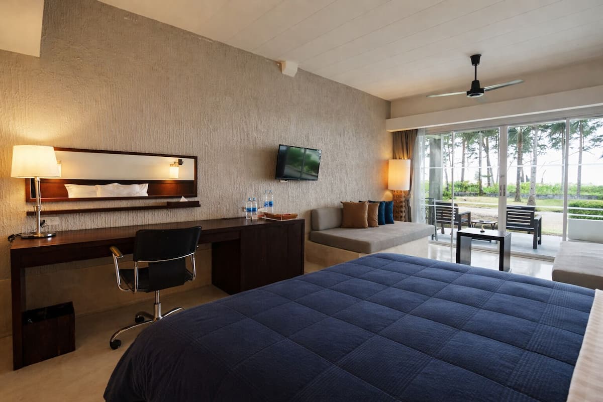 Ein Hotelzimmer mit Bett, Schreibtisch, Stuhl, Fernseher und einem Balkon mit Sitzgelegenheit.