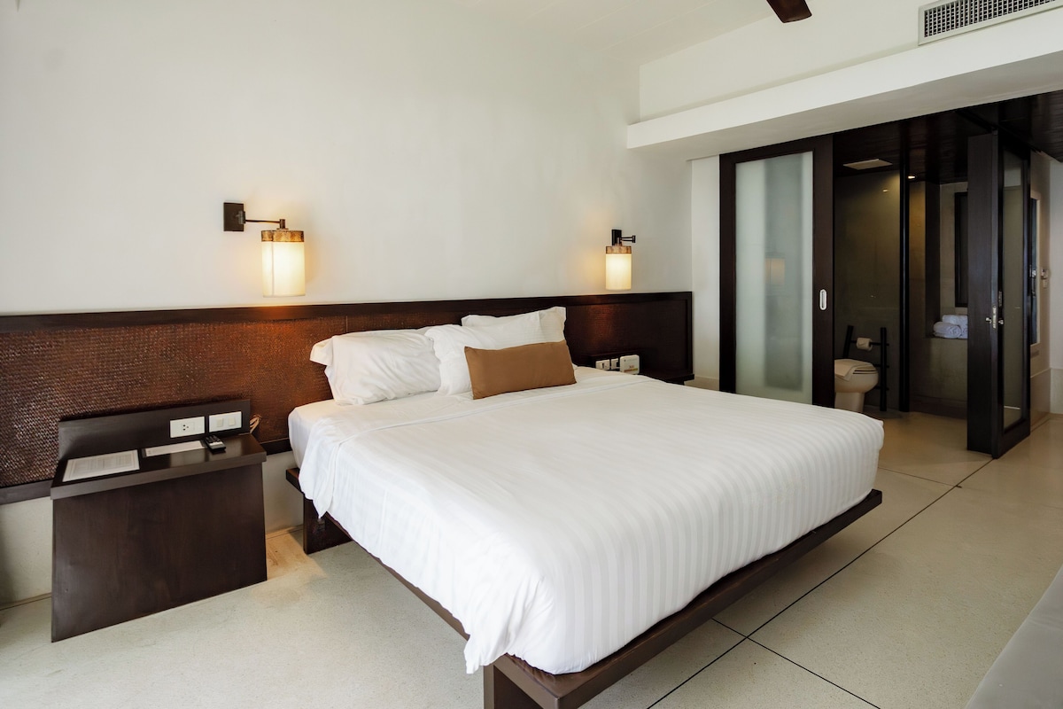 Une chambre d’hôtel moderne avec un grand lit, des tables de chevet et une porte coulissante donnant accès à la salle de bain.