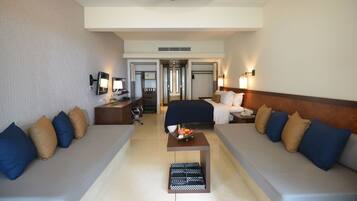 Habitación de hotel con una cama grande, dos sofás, una mesita con un frutero y un escritorio con una lámpara.