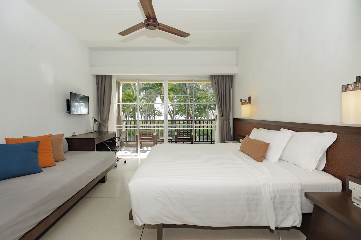 Une chambre d’hôtel comprenant un lit, un canapé, une télévision, un ventilateur de plafond, une fenêtre avec des rideaux et une table de chevet.