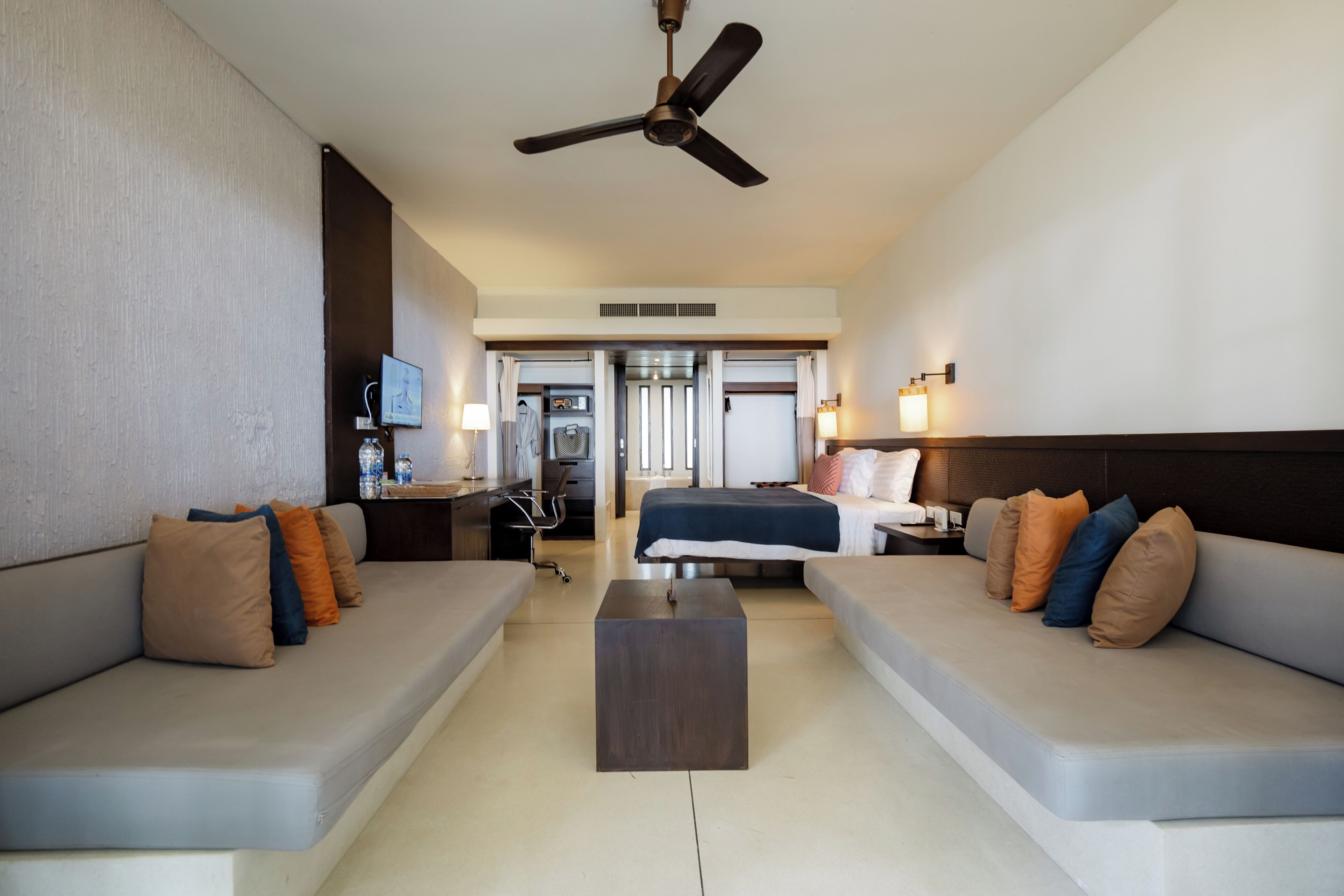 A modern hotel room with a sofa, a bed, a desk, and a ceiling fan.