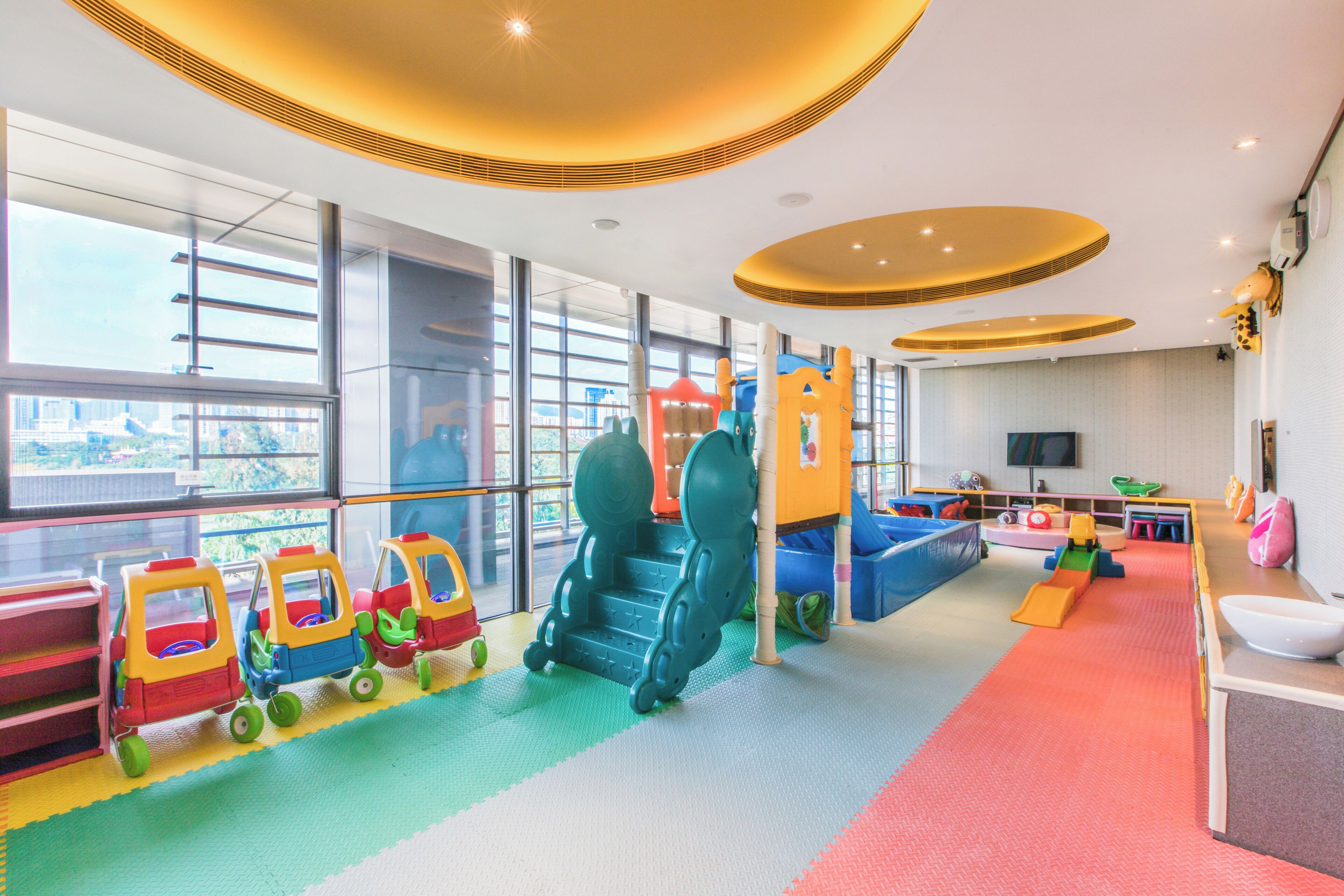 A children's play area with colorful play structures and a large window offering a view of the city.