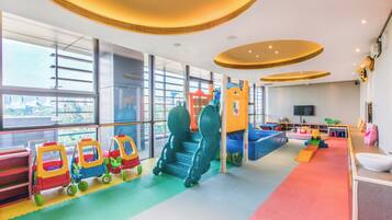 A children's play area with colorful play structures and a large window offering a view of the city.