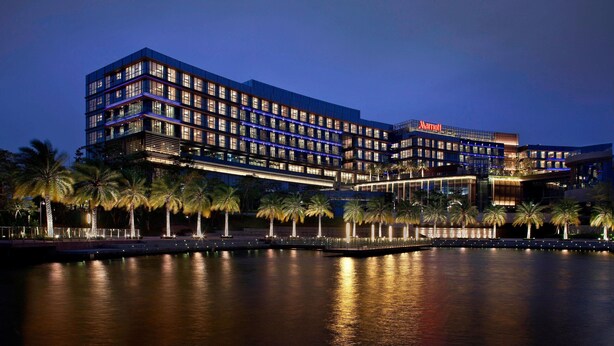 A multi-story hotel with a Marriott sign, featuring a waterfront view and palm trees along the promenade. - The Oct Harbour, Shenzhen - Marriott Executive Apartments (Shenzhen)