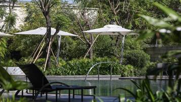 A poolside area with lounge chairs, umbrellas, and lush greenery.