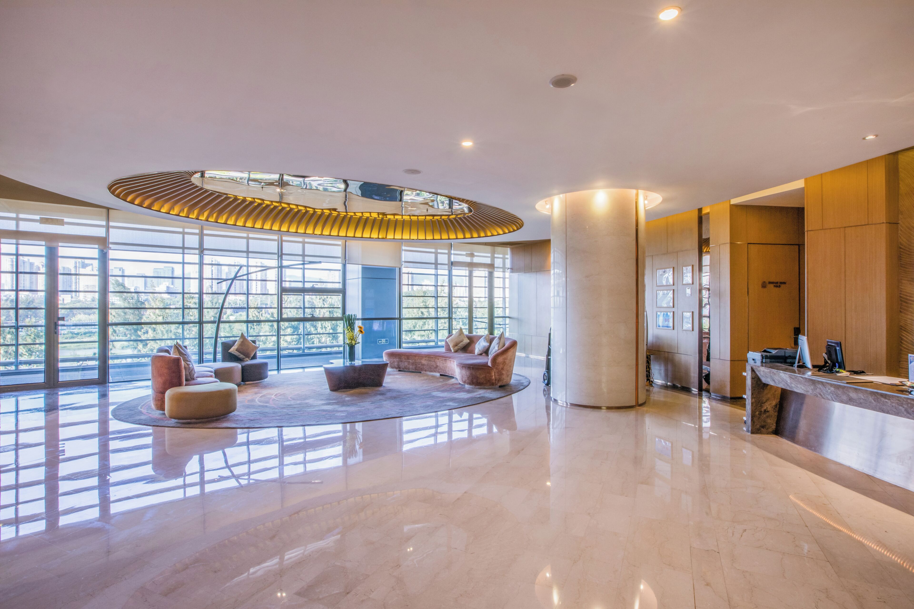 Eine großzügige Lobby mit hoher Decke, großen Fenstern und einer zentralen Sitzecke mit Sofas und einem Couchtisch.