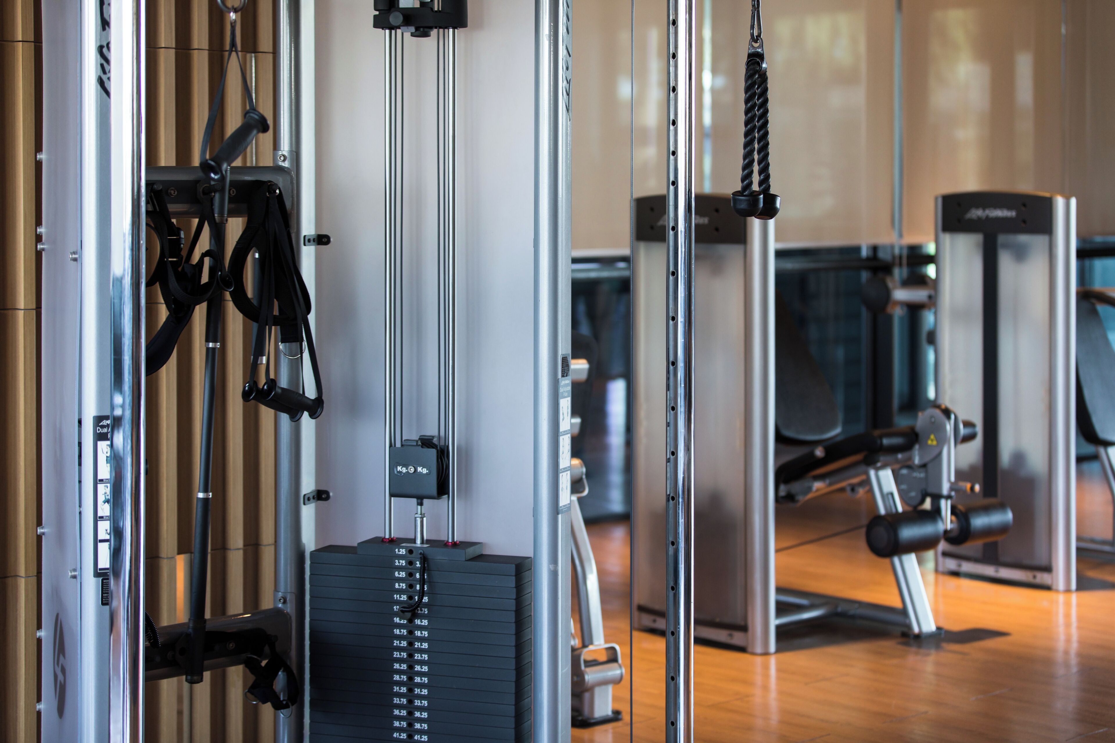 Ein Fitnessstudio mit verschiedenen Trainingsgeräten, darunter ein Kabelzuggerät und ein Gewichtsstapel.