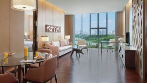 A modern hotel room with a dining area, a sofa, a TV, and a large window offering a city view. - The Oct Harbour, Shenzhen - Marriott Executive Apartments (Shenzhen)