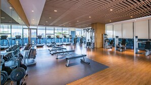 A modern gym with various exercise equipment, large windows, and a wooden ceiling. - The Oct Harbour, Shenzhen - Marriott Executive Apartments (Shenzhen)