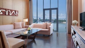 A modern living room with a sofa, a glass coffee table, and a television on a wooden console. A large window offers a view of a body of water and distant cityscape. - The Oct Harbour, Shenzhen - Marriott Executive Apartments (Shenzhen)