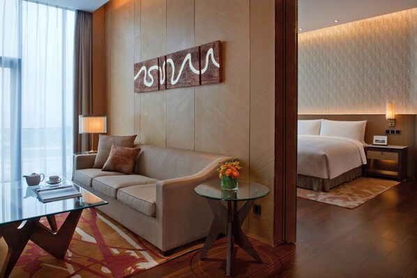 A modern hotel room with a sofa, a glass coffee table, a bed, and a wall-mounted artwork. - The Oct Harbour, Shenzhen - Marriott Executive Apartments (Shenzhen)