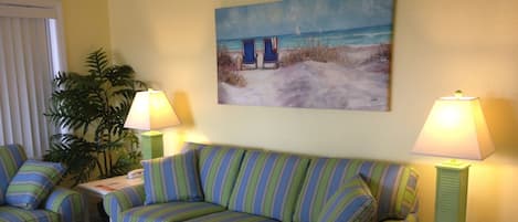 A living room with a striped sofa, two side tables with lamps, a coffee table, and a painting of a beach scene on the wall.