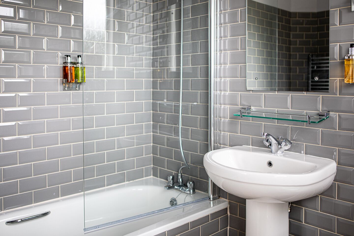 A modern bathroom with a white sink, a glass shower enclosure, and grey tiled walls.