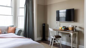 A hotel room with a bed, a desk with a chair, a flat-screen TV, and a window with curtains.