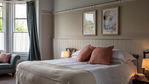 A bedroom with a large bed, two bedside lamps, a chair, and two framed artworks on the wall. - Burrator Inn (Yelverton)