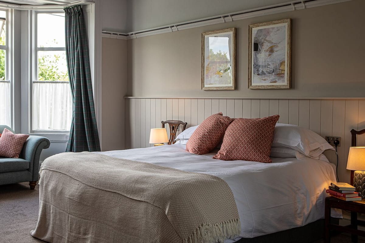 A bedroom with a large bed, two bedside lamps, a chair, and two framed artworks on the wall.
