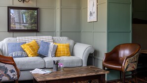 A living room with a grey sofa, yellow and blue pillows, a wooden coffee table, a brown leather armchair, and wall-mounted lamps. - Burrator Inn (Yelverton)