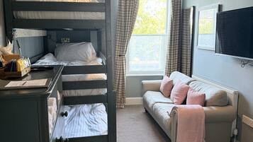 Una cama individual con escritorio y silla, un sofá, una ventana con cortinas y una lámpara colgante.