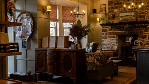 A cozy room with a wooden cabinet, a cushioned chair, a fireplace, and a stone wall. - Burrator Inn (Yelverton)