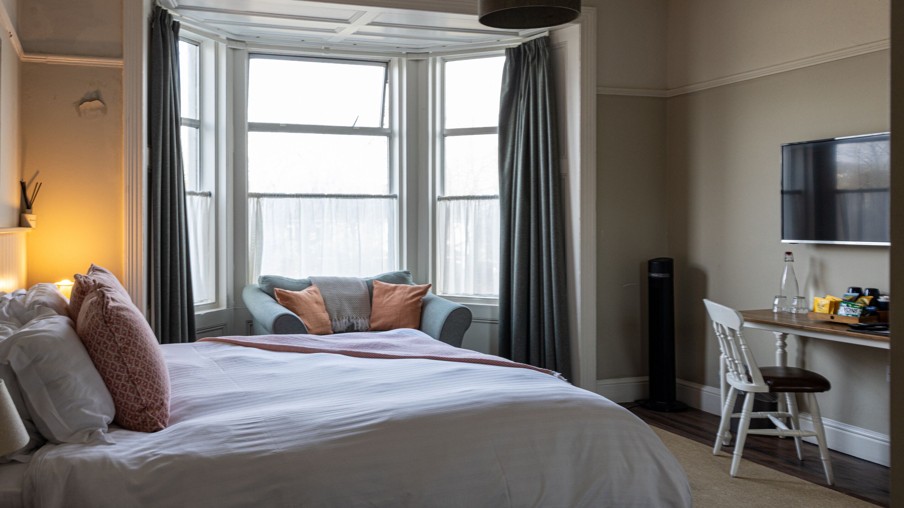 A hotel room with a large bed, a desk with a chair, and a television on the wall.