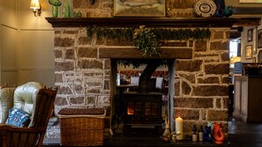 A stone fireplace with a mantel decorated with greenery, a lit candle, and a rustic wooden chair with a cushion. - Burrator Inn (Yelverton)