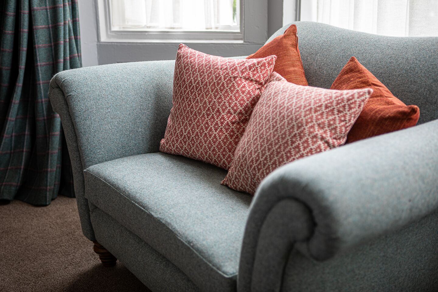 A grey sofa with patterned cushions in a room with a window and curtains.
